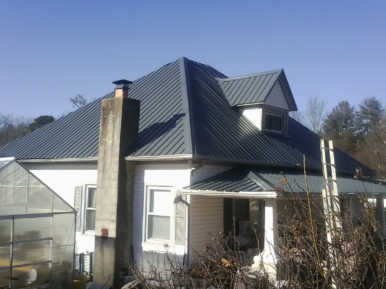 Dark blue standing seam metal roof on a white farmhouse with dormer — Slate & Tile Roof Repair by Roofing Brothers in High Shoals