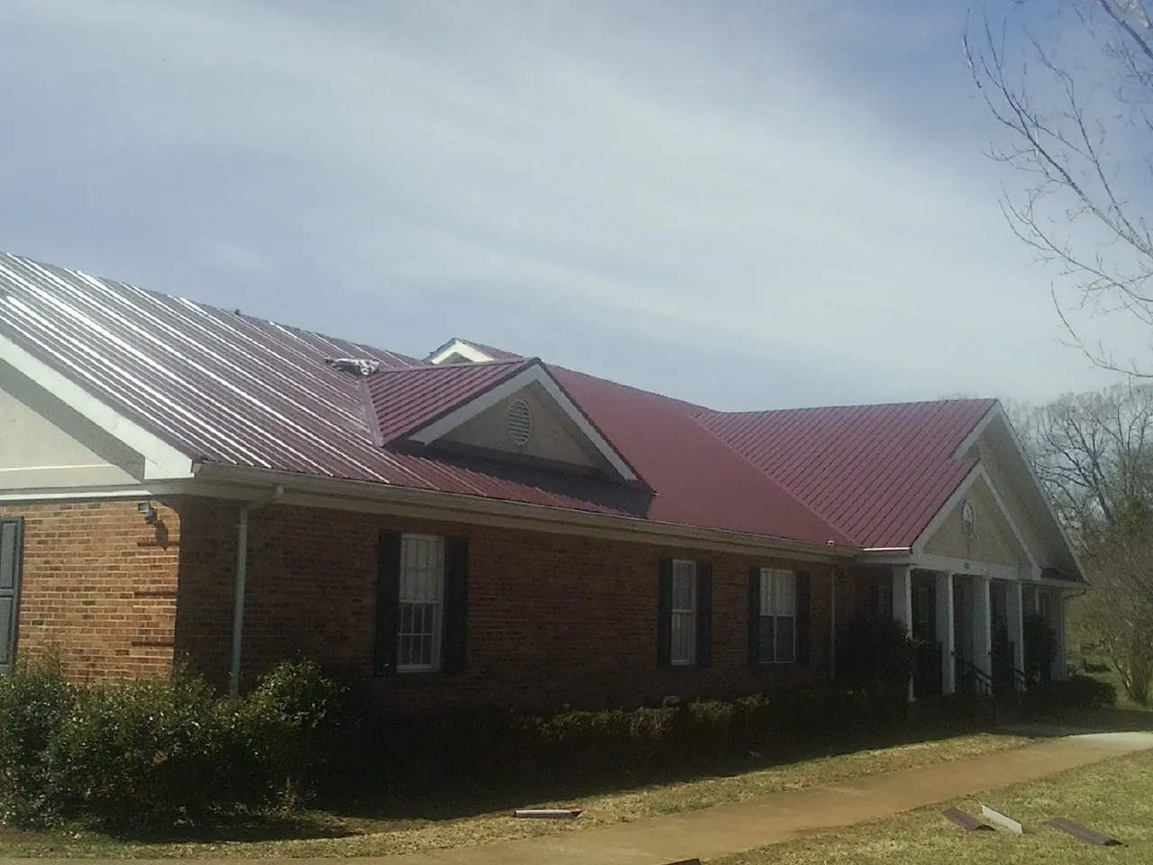 Red metal roof with gabled entries on a long brick building, from a Hail Damage Roof Repair job in High Shoals