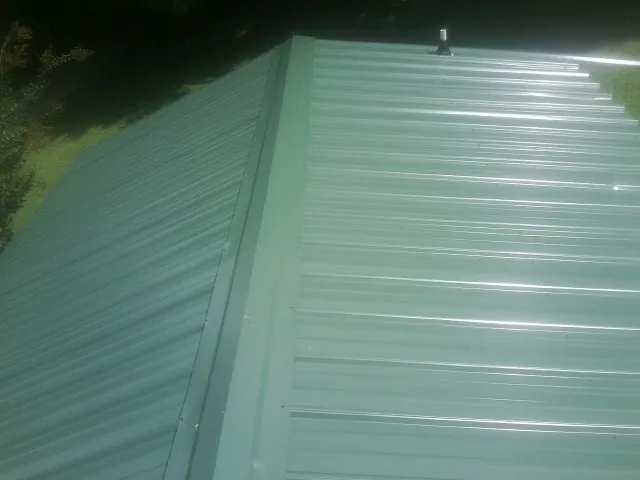 New green metal panels meeting at the ridge of a roof — Flat Roof Repair work by our crew in High Shoals