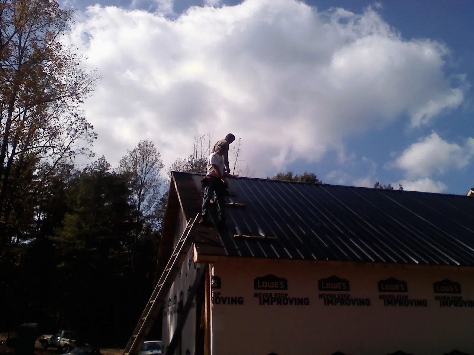 Roofer fastening dark metal panels high against a cloudy sky, from a Roof Inspection job in High Shoals
