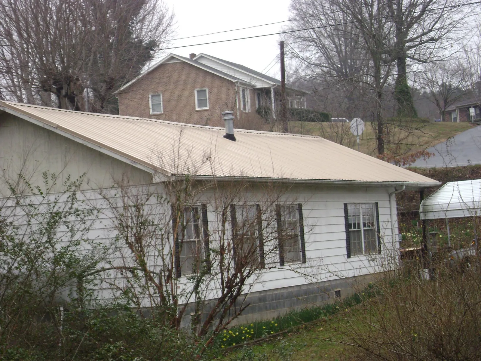 Tan metal roof on a white sided house set into a hillside — Commercial Roofing by Roofing Brothers in High Shoals